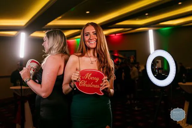 two women posing for a 360 photo booth in a holiday party while holding christmas themed props