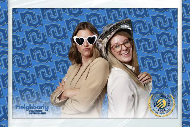 two women posing for a green screen photo booth in a corporate event with a branded backdrop