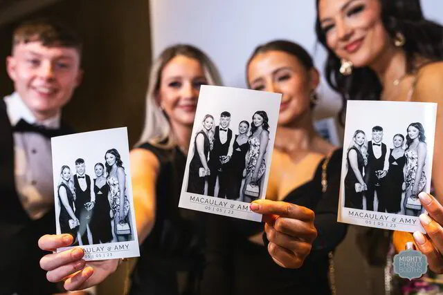 four people holding prints of a black and white photo booth in a wedding
