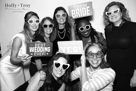 seven women posing for a black and white photo booth in a wedding while holding wedding themed props