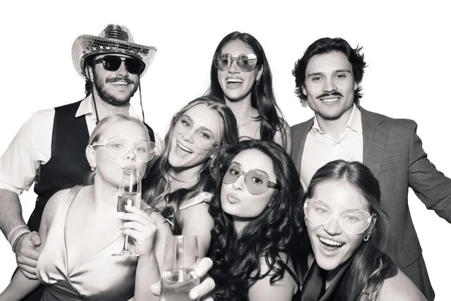 seven people wearing props posing for a black and white photo booth in a wedding in austin texas