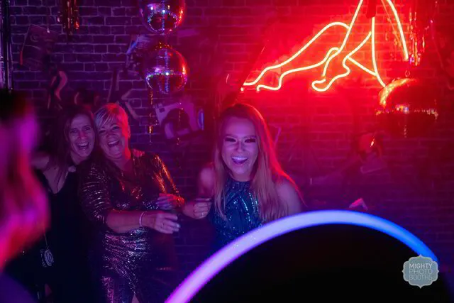 three women smiling and laughing while posing for a roaming photo booth in a social event